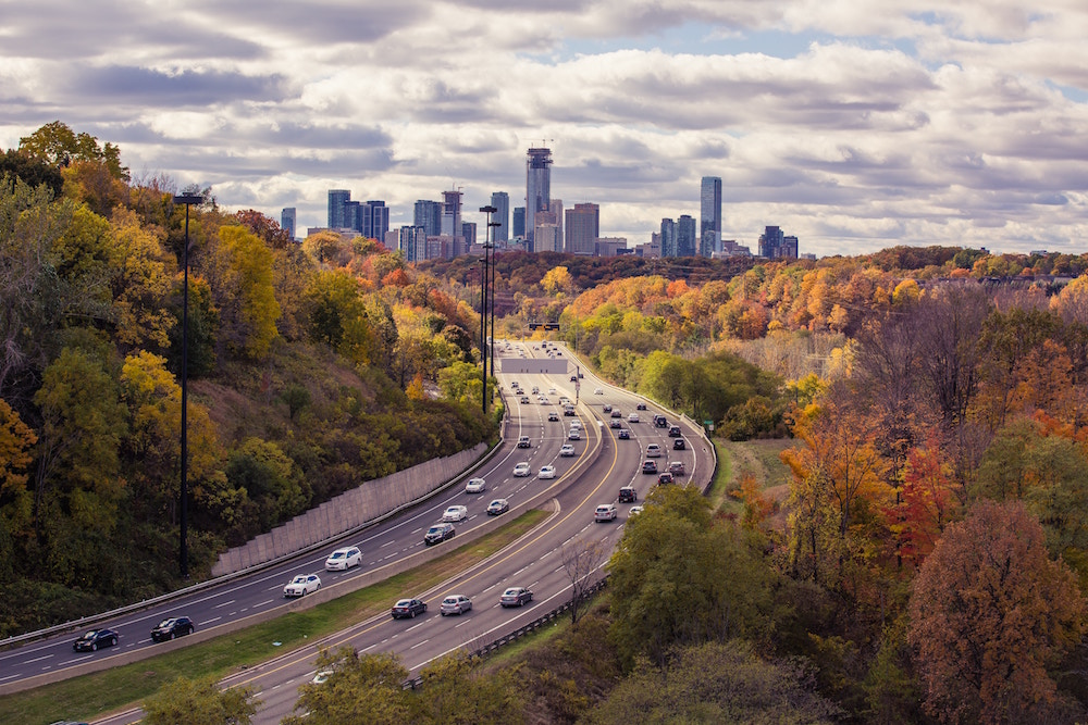 green and yellow trees with highway leading toward Toronto skyline