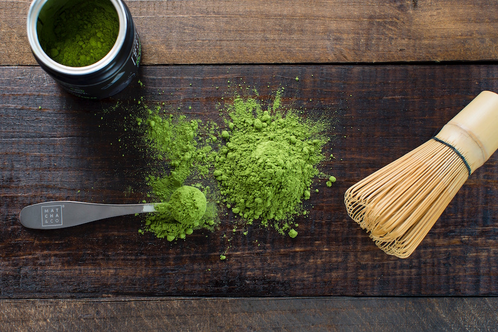 Chasen whisk and green matcha powder on wooden surface