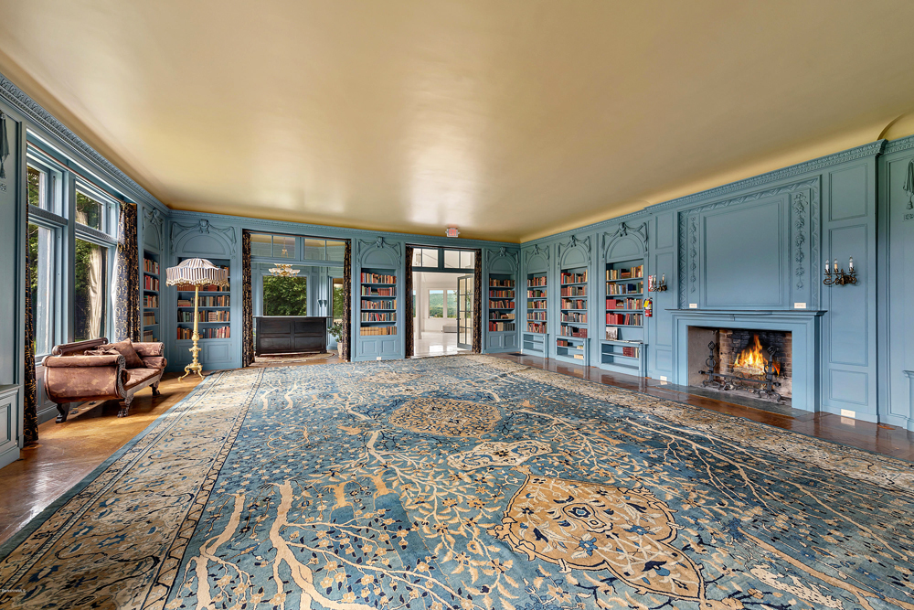 A large pastel blue library with plenty of natural light with a wood-burning fireplace and oversized area rug