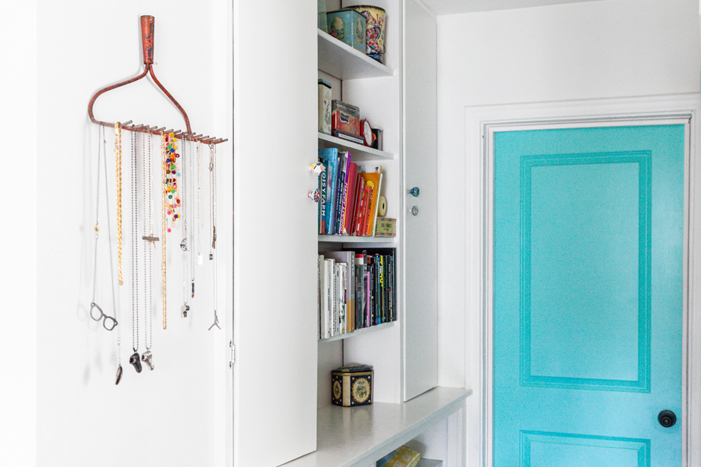 A white room with a turquoise door and vertical bookshelf