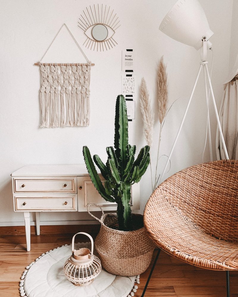 vintage furniture including a wicker chair, a handwoven basket holding a cactus, a lantern atop a soft rug and a shabby-chic dresser.