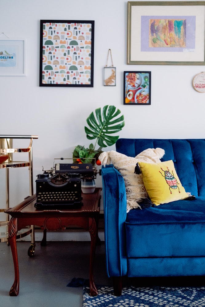 living room with blue couch and vintage table, typewriter and wall art