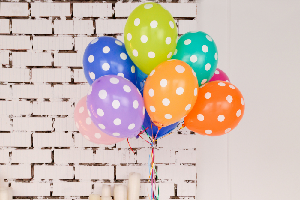 Colourful polka dot balloons in front of a white brick fireplace