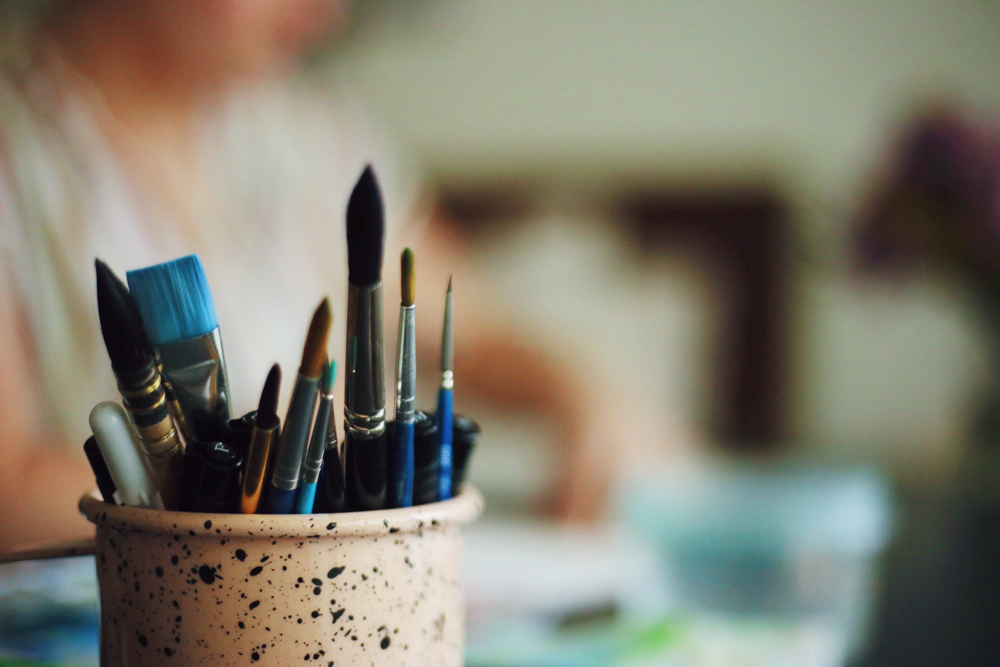 A ceramic holder with various markers and paint brushes