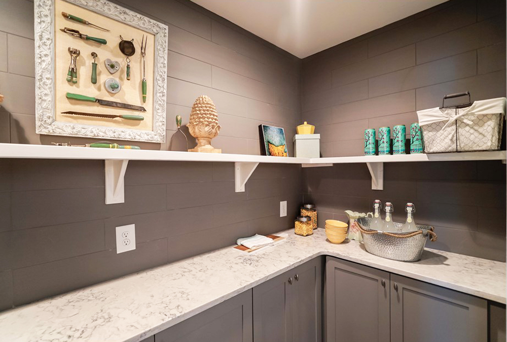 A small, windowless grey walk-in pantry with narrow countertops and plenty of storage and open-shelving