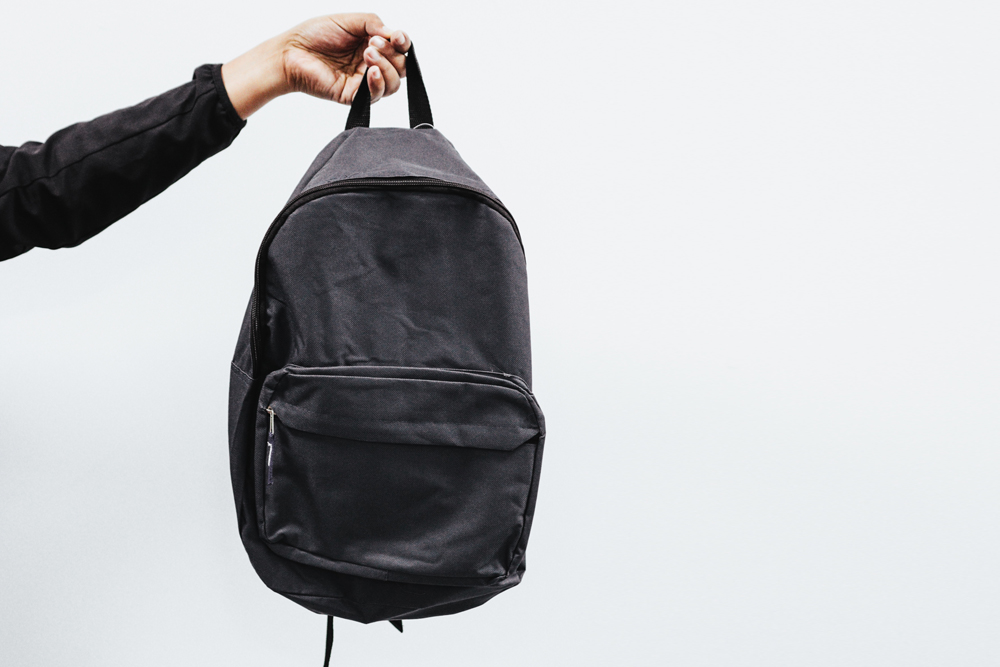 person holding dark backpack in the air