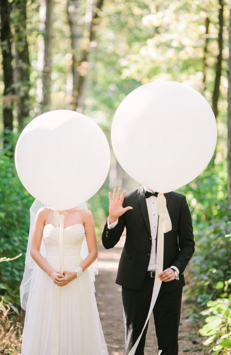 Newlyweds cover their faces with big white balloons during a photoshoot