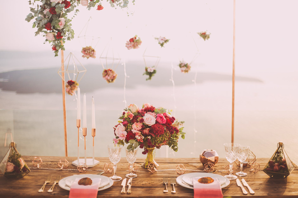 Head table at a wedding featuring hanging decor and a variety of candles facing a waterfront view