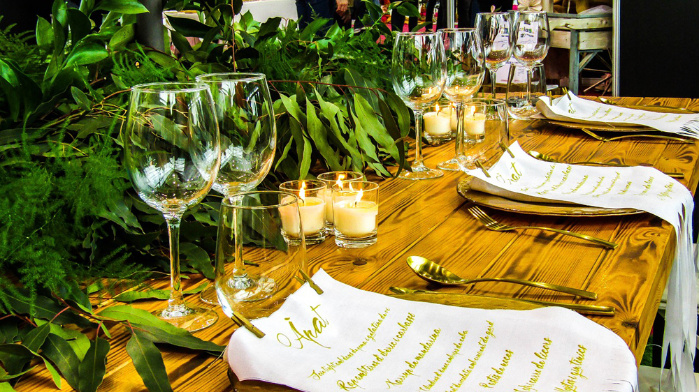 Head table at a wedding with green foliage, candles and gold cutlery