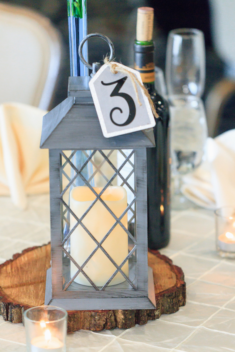 A rustic lantern on a guest table at a wedding on top of a circular piece of wood