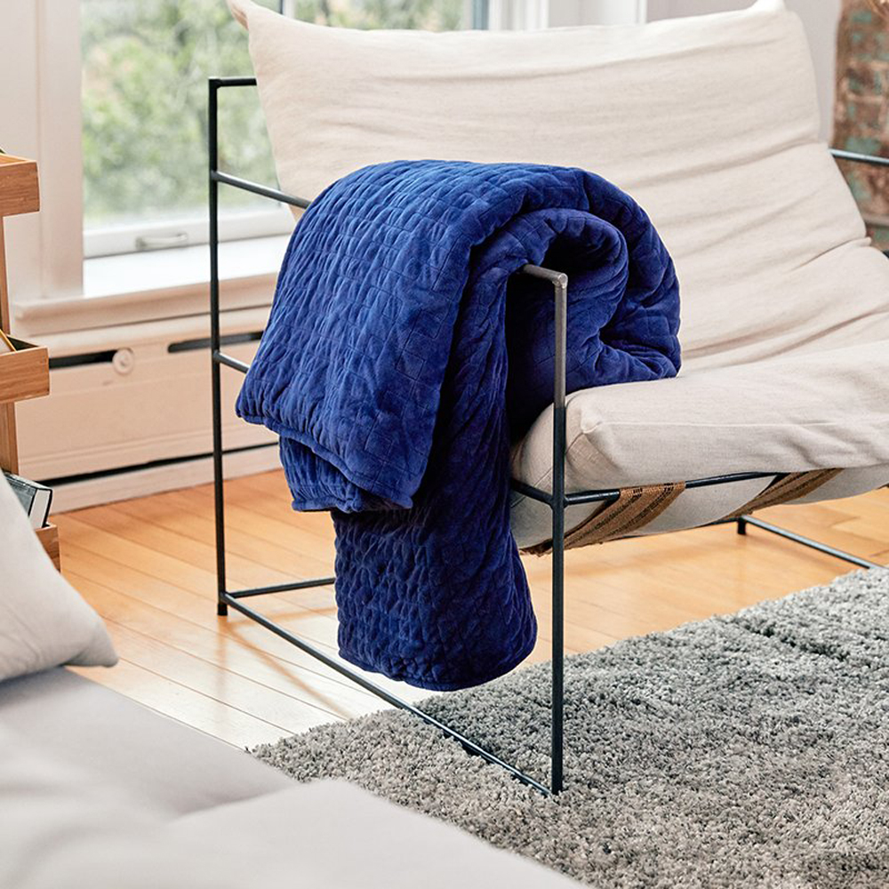 A blue weighted blanket covering a modern chair in a living room