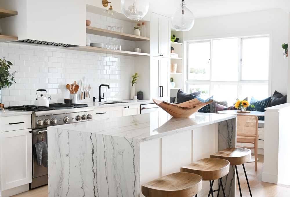 A white kitchen with a waterfall island (with heavy veining) and wood-topped stools