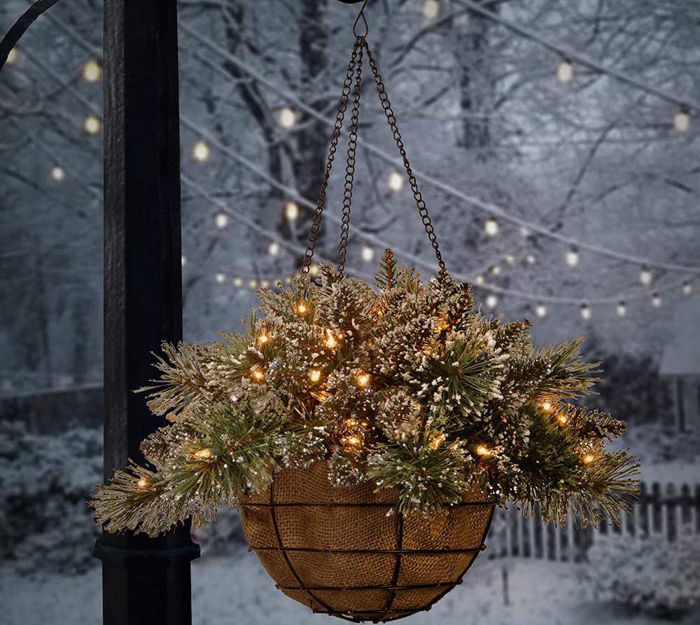 hanging basket with lights and snow-tipped pine branches on porch in snowy backyard