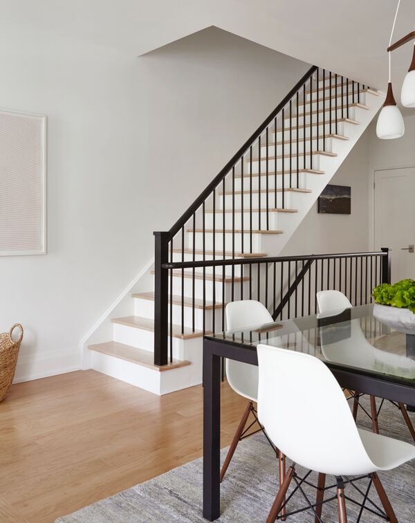 white staircase with pale wood steps and black vertical banister and railings, dining room chairs and table in right foreground