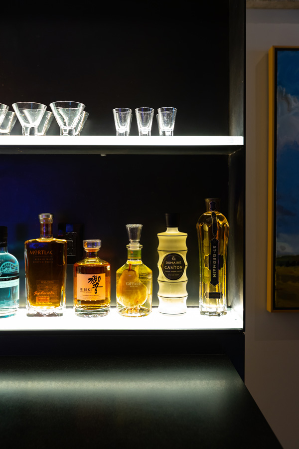 close up of custom bar with bottles on lower lit shelf and glasses on top shelf