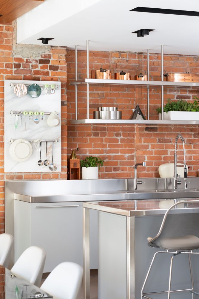 exposed brick wall kitchen, hanging utenils, stainless steel counter tops and and island, copper pots on top shelf