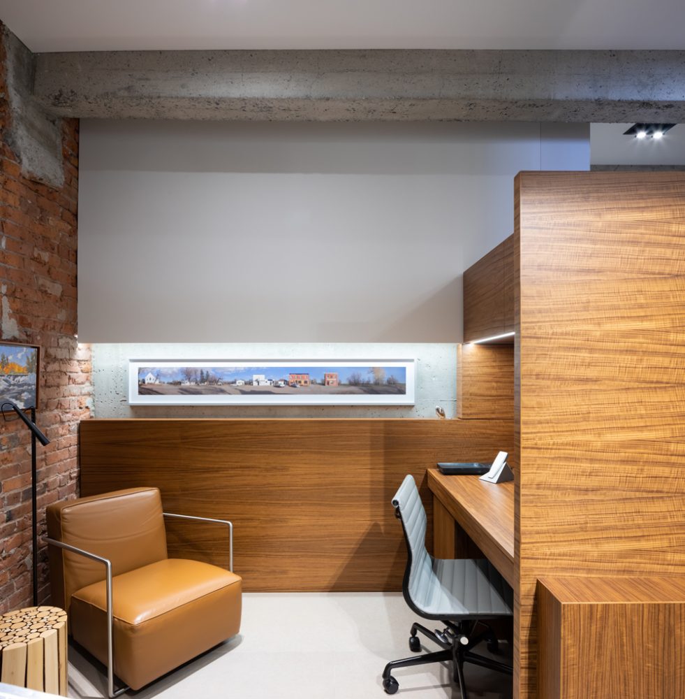modern home office with walnut custom cabinetry, tan leather chair in left corner, concrete beams, two paintings