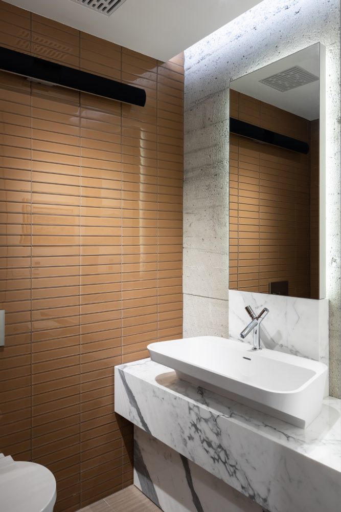 bathroom with raised sink, veined marble vanity, tan glass tiles on left wall
