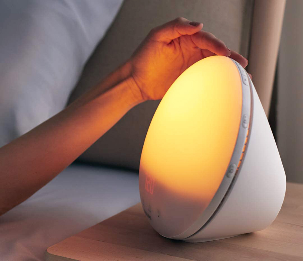 A woman's hand reaches for a light alarm clock on her nightstand
