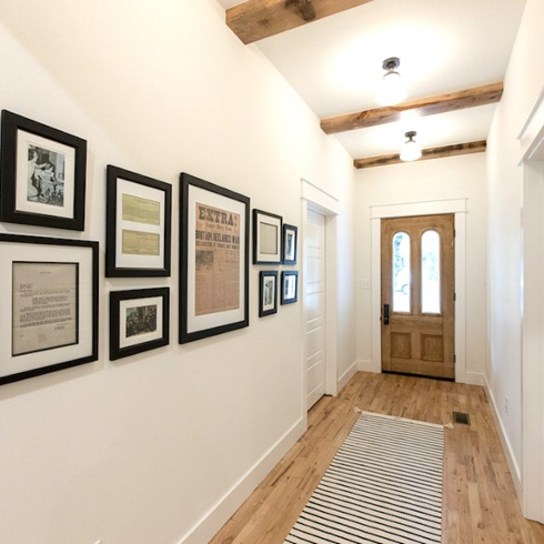 Beautiful hallway with vintage front doors with glass panes, wood floors, a black and white runner, exposed beams on the ceiling and a black art gallery wall as seen on Fixer to Fabulous on HGTV Canada