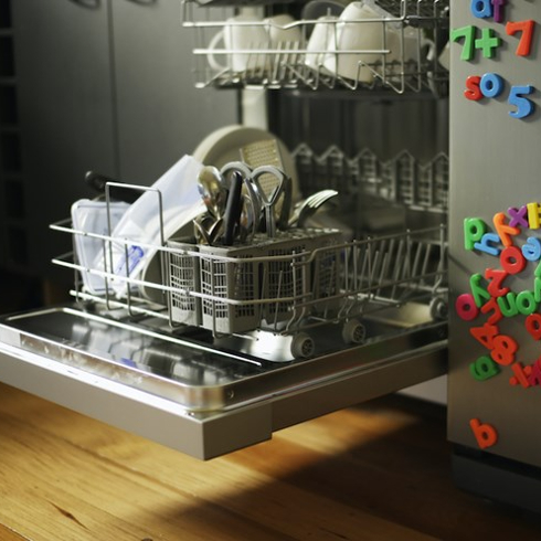 Dishwashing machine with open drawer next to refrigerator covered in children’s fridge magnets