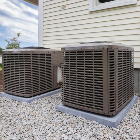 Two air-conditioning units side-by-side in the backyard of a house