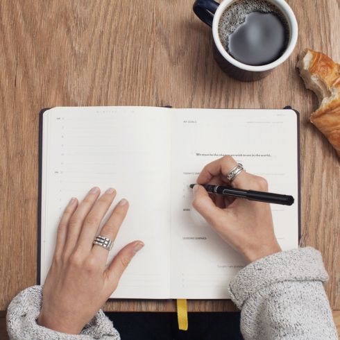 Woman writing in notebook on desk with croissant and coffee