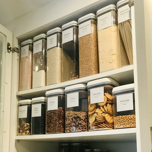 An organized kitchen cabinet with plastic containers that are labelled