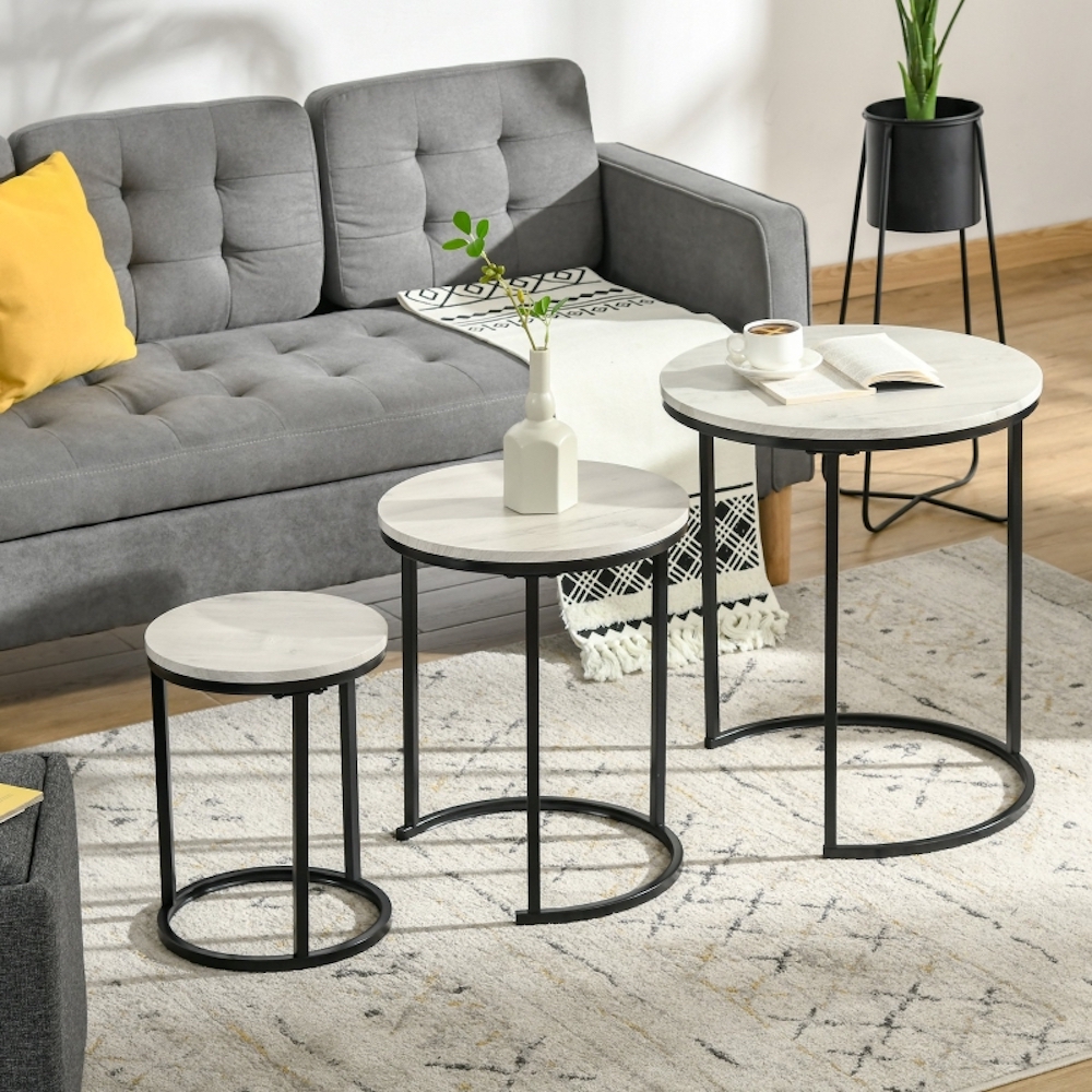 Three Homcom Round Nesting Coffee Tables with black frame and white ceramic tops sit on top of a white rug in front of a grey couch with a yellow throw pillow