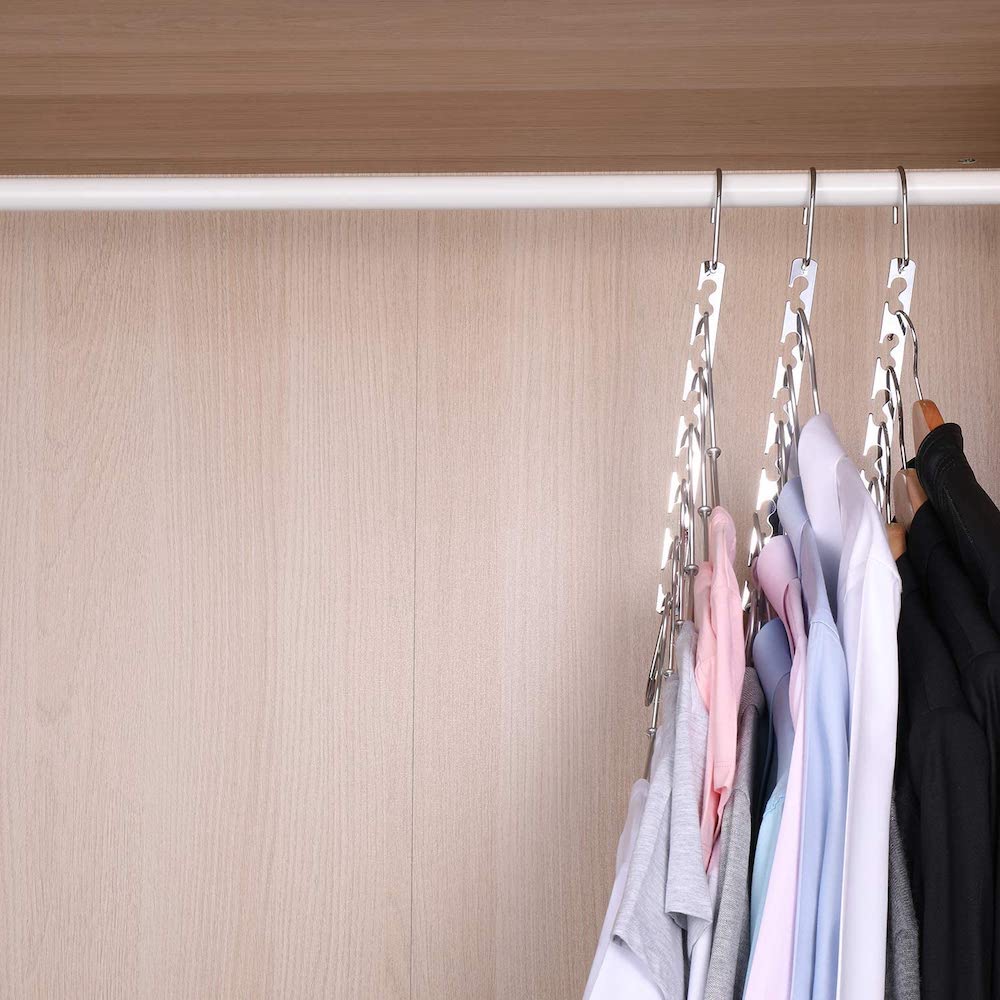 Three Bloberey Space Saving Hangers hang in a wood closet with many multicoloured and black button-up shirts on hangers hanging from them