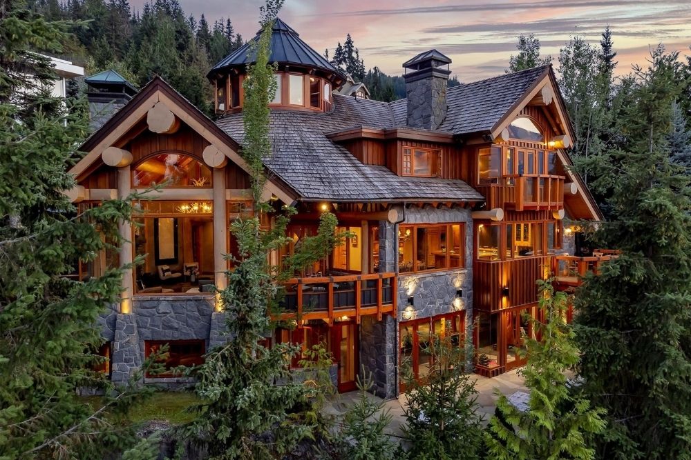 A luxury wooden cottage with multiple floors and big green trees.