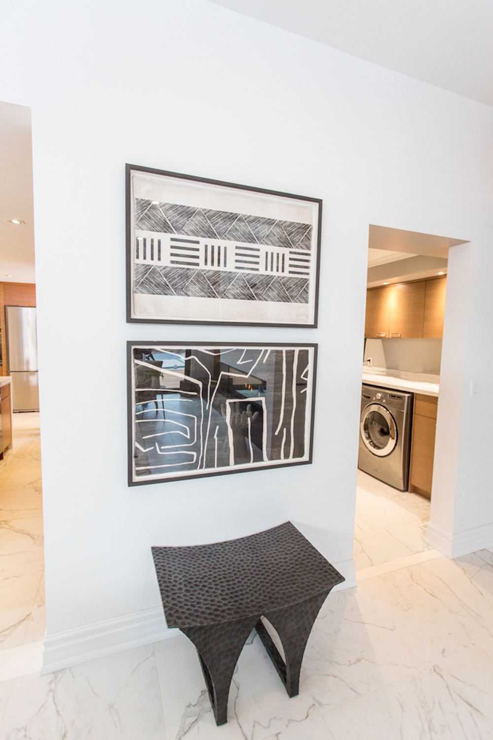 A white wall with two black and white framed pieces of art and black curved bench in a house designed by Sarah and Bryan Baeumler as featured on HGTV Canada