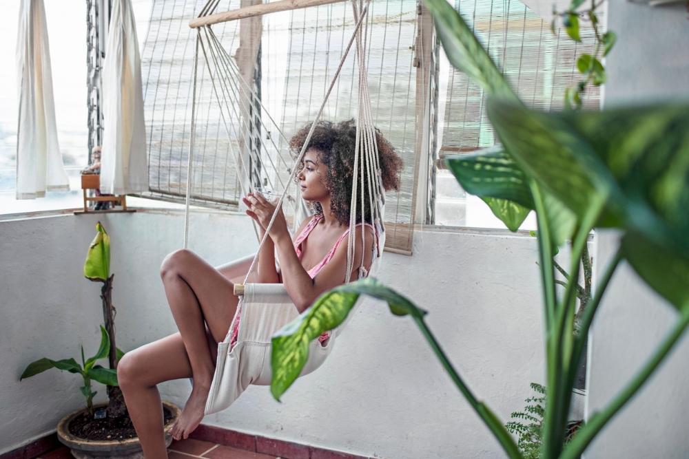 Woman sipping coffee in an indoor swing, surrounded by plants