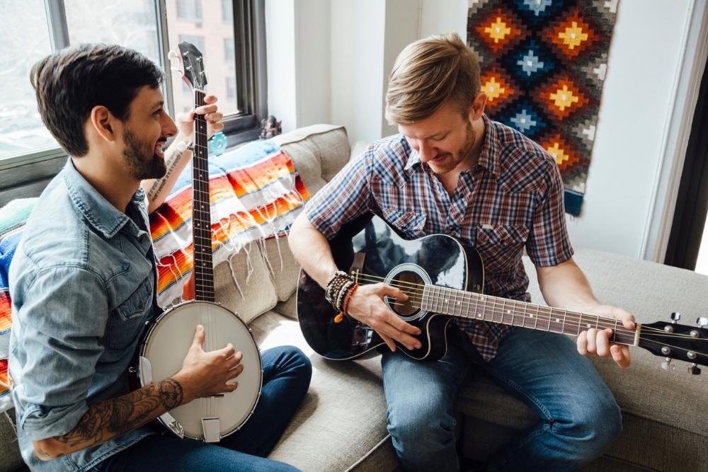 Two friends playing a banjo and a guitar in their music room