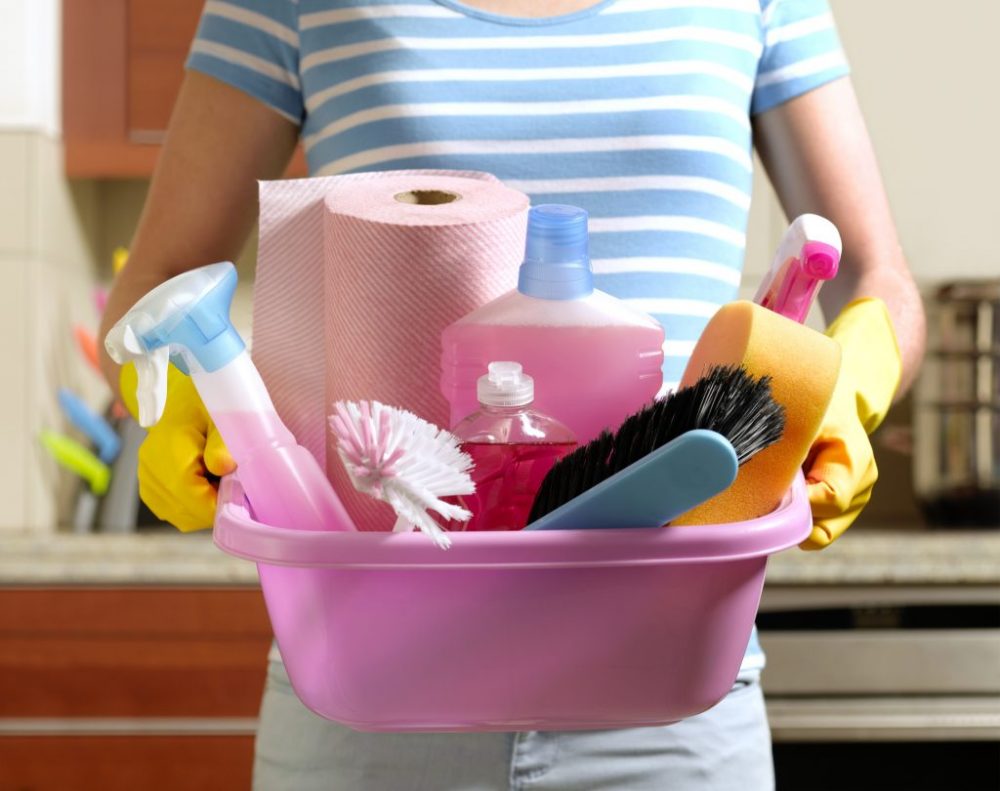 Woman holding a bin of cleaning tools and products.
