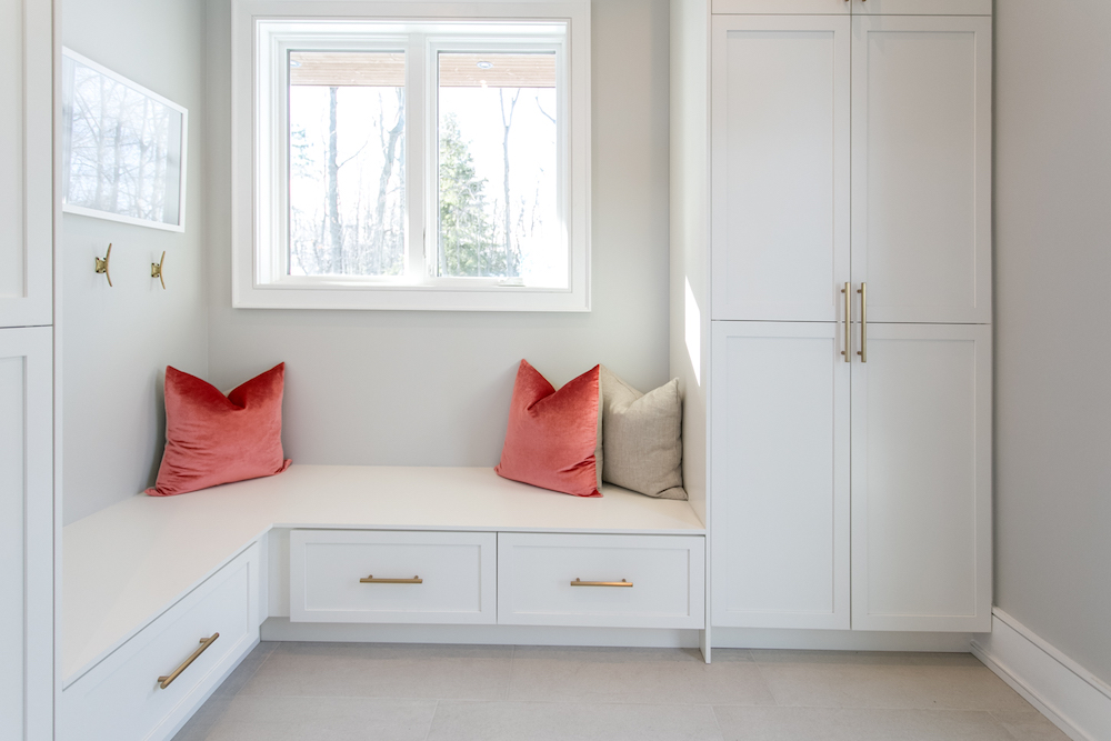 White functional mudroom with lots of storage and a pretty corner bench with white and gold finishes and pops of rose and beige in the throw pillows all add a modern touch as featured on HGTV Canada