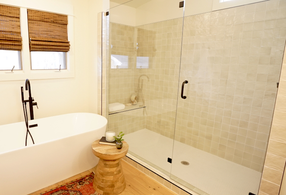 Spa like bathroom with gold and black fixtures, wood floors, handmade tile, deep standalone white bathtub and large walk in shower as seen on Fixer to Fabulous on HGTV Canada