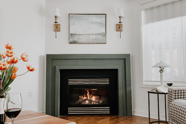 Courtney's DIY fireplace installed and painted a moody green, paired with elegant accents like gold sconces and framed art.