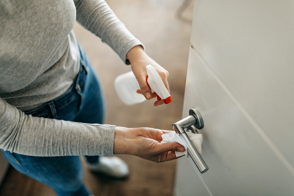 Woman disinfects door handle with spray bottle and cloth