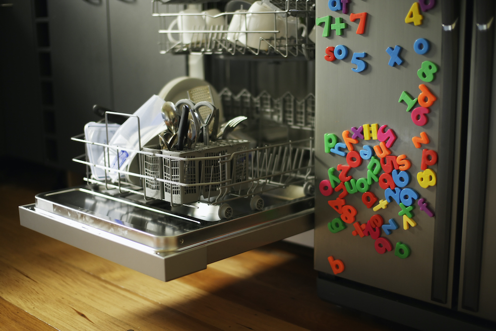 Dishwashing machine with open drawer next to refrigerator covered in children’s fridge magnets