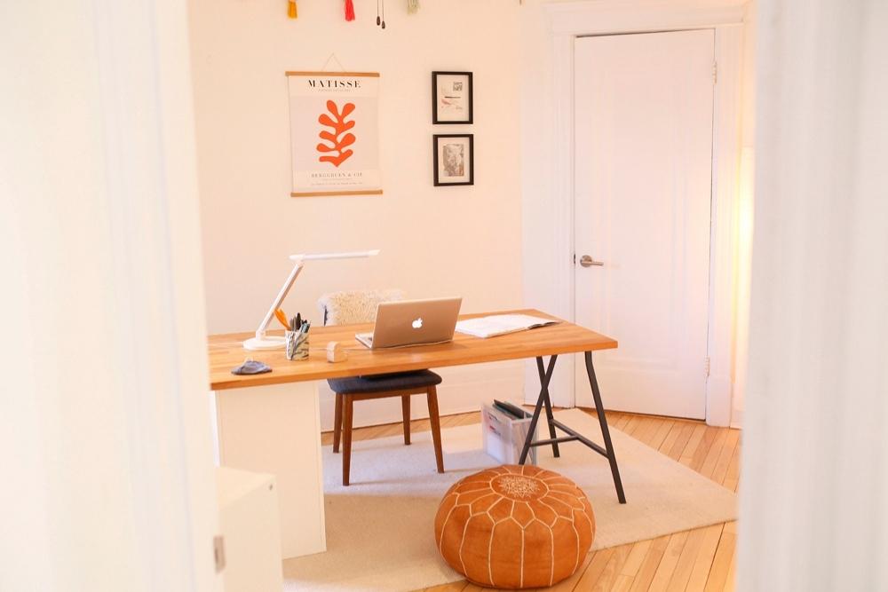 A white minimal office with a wooden desk and three pieces of art on the wall.