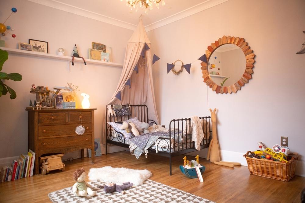 A cozy and whimsical child's room with hardwood floors, a single black iron bed, and toys on the ground.