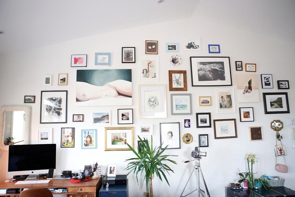 An office with a gorgeous gallery wall filled with several different photos and pieces of art in various coloured-picture frames