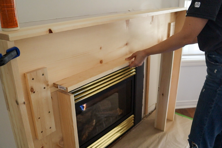 Courtney adding boards around the perimeter of the fireplace to make the mantle stick out from the wall and frame the actual fireplace area.