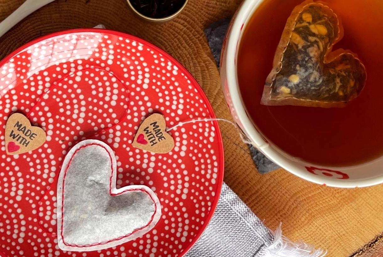 A heart-shaped tea bag on a red and white plate with a cup of tea