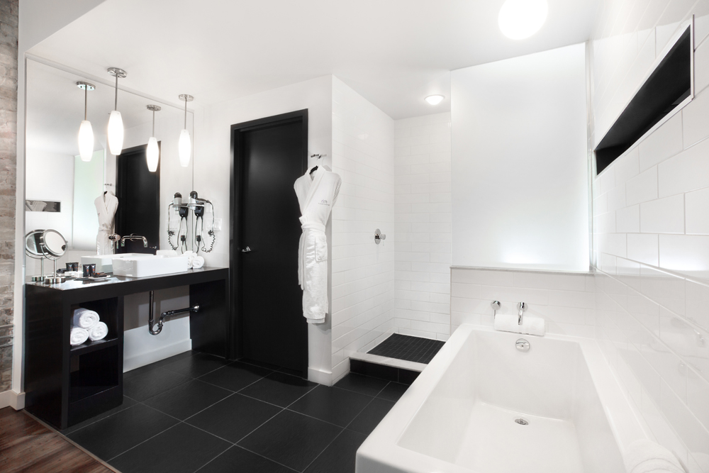open bathroom with black floor tiles, rectangular tub on right and white robe on hanger by shower