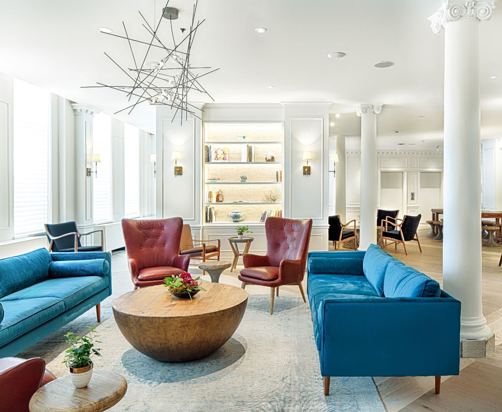 lounge with two bright blue sofas, red leather wingback chairs, round wooden coffee table, white pillars