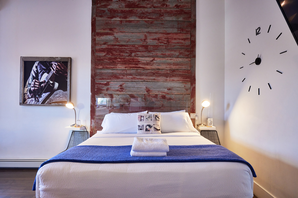 bed with blue blanket, distressed red wood and clock on wall
