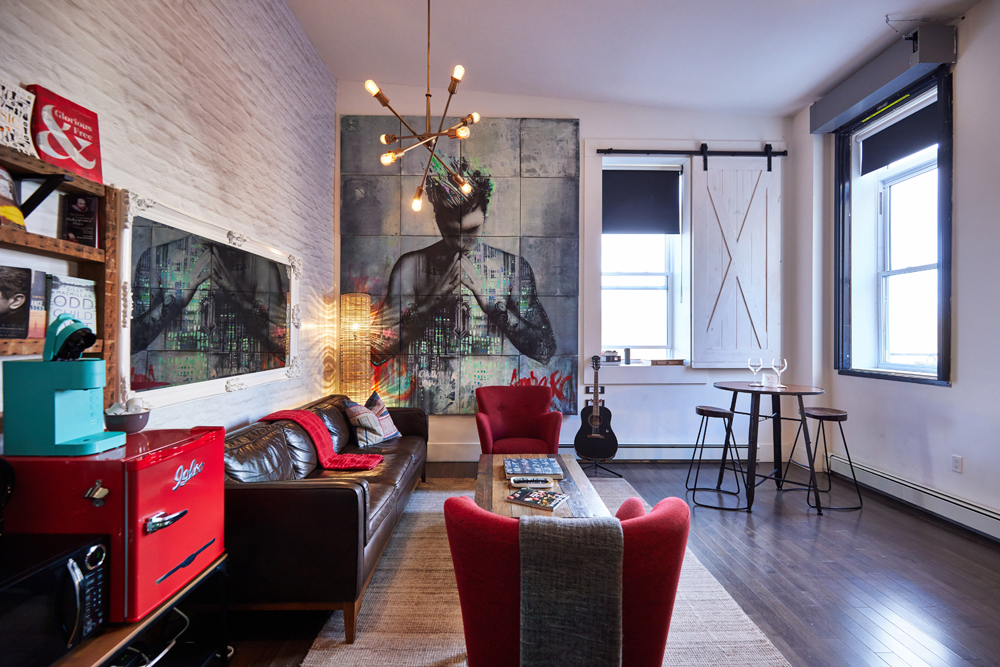 lounge area with small red fridge left, two red chairs, mural of bieber on back wall