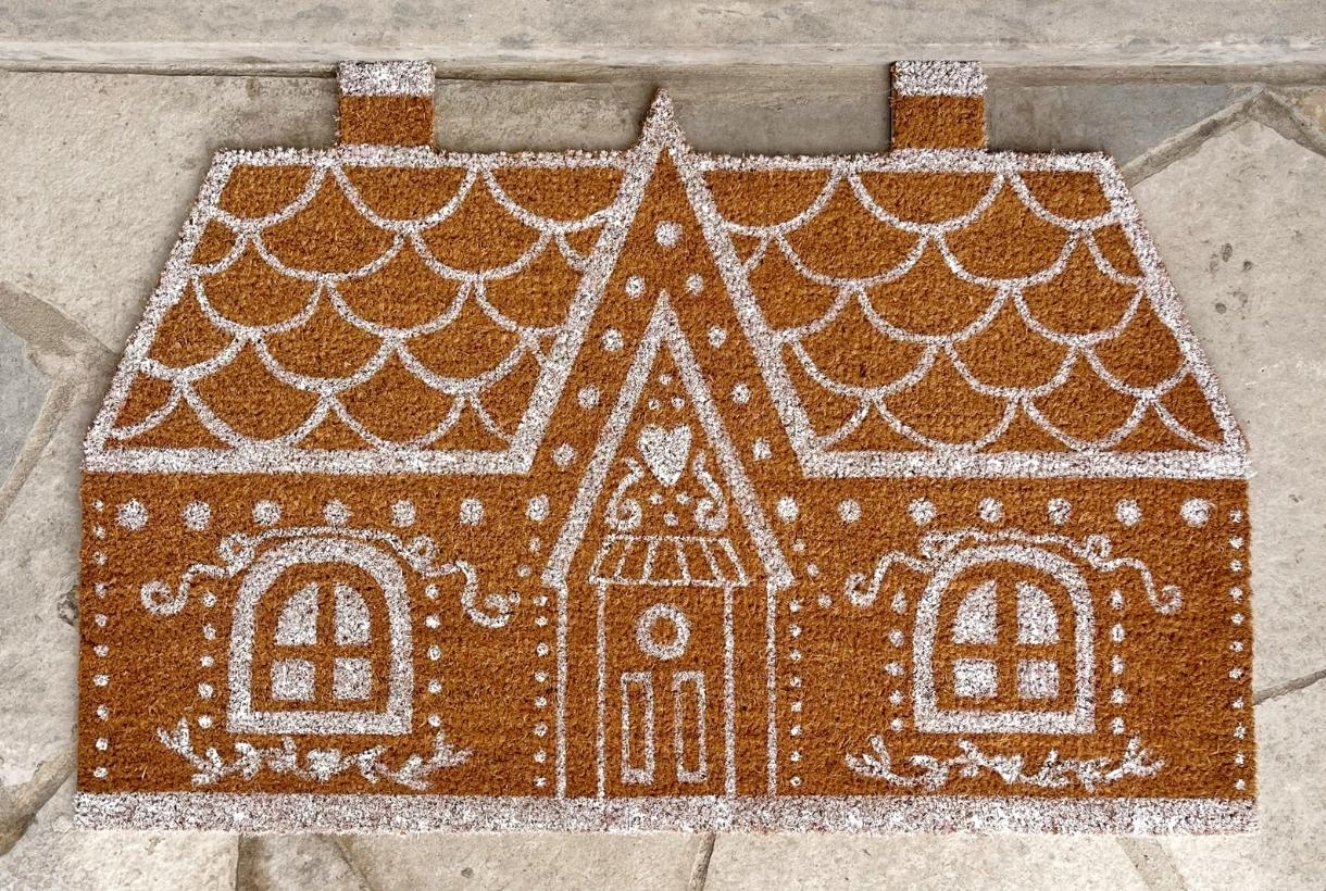 A gingerbread house doormat on a porch.